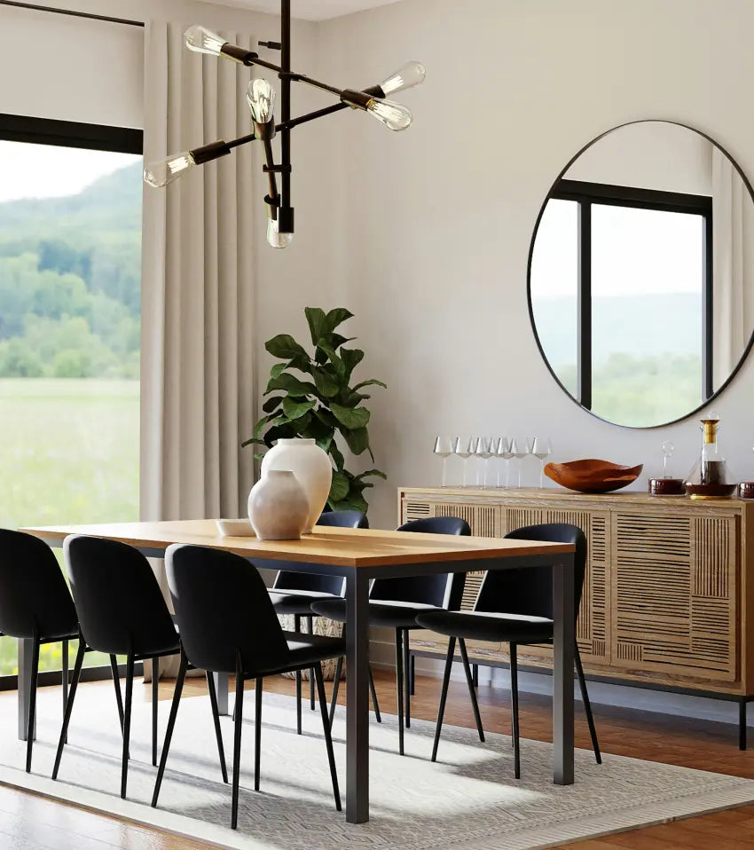 Modern dining room with a wooden table and six black chairs, a sideboard with glassware and decor, a round wall mirror, large windows with beige curtains, and a black chandelier overhead.