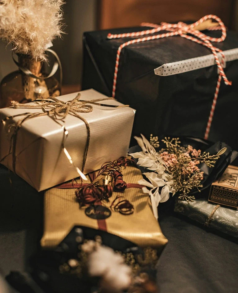 Beautifully wrapped gift boxes in gold, black, and patterned paper with ribbons and dried floral decorations on a table.