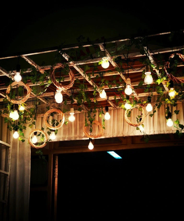 Hanging string lights with warm bulbs and decorative vine greenery on a wooden trellis, accented with woven circular ornaments.