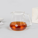 Clear glass teapot with amber liquid on a light gray background