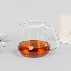 Clear glass teapot with amber liquid on a light gray background