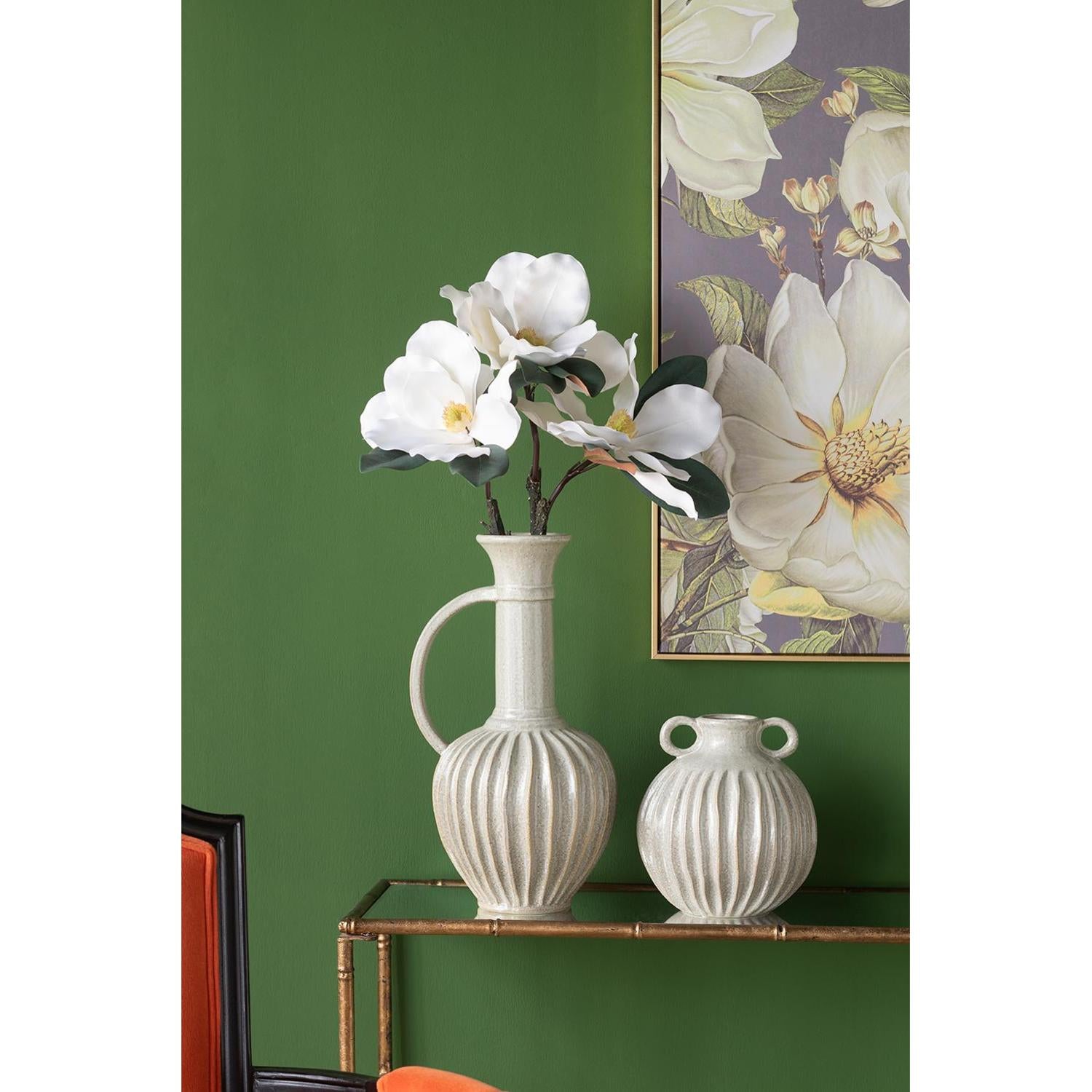 Two white vases with floral design on a green wall with a floral painting.