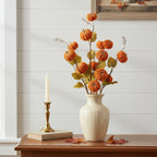 Decorative arrangement with pumpkins in a vase on a wooden surface, candle, and book in the background.