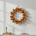 Decorative wreath with pumpkins on a white wall with a candle and leaves on a table.
