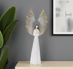 Decorative angel sculpture on a wooden surface with a gray wall and plant in the background