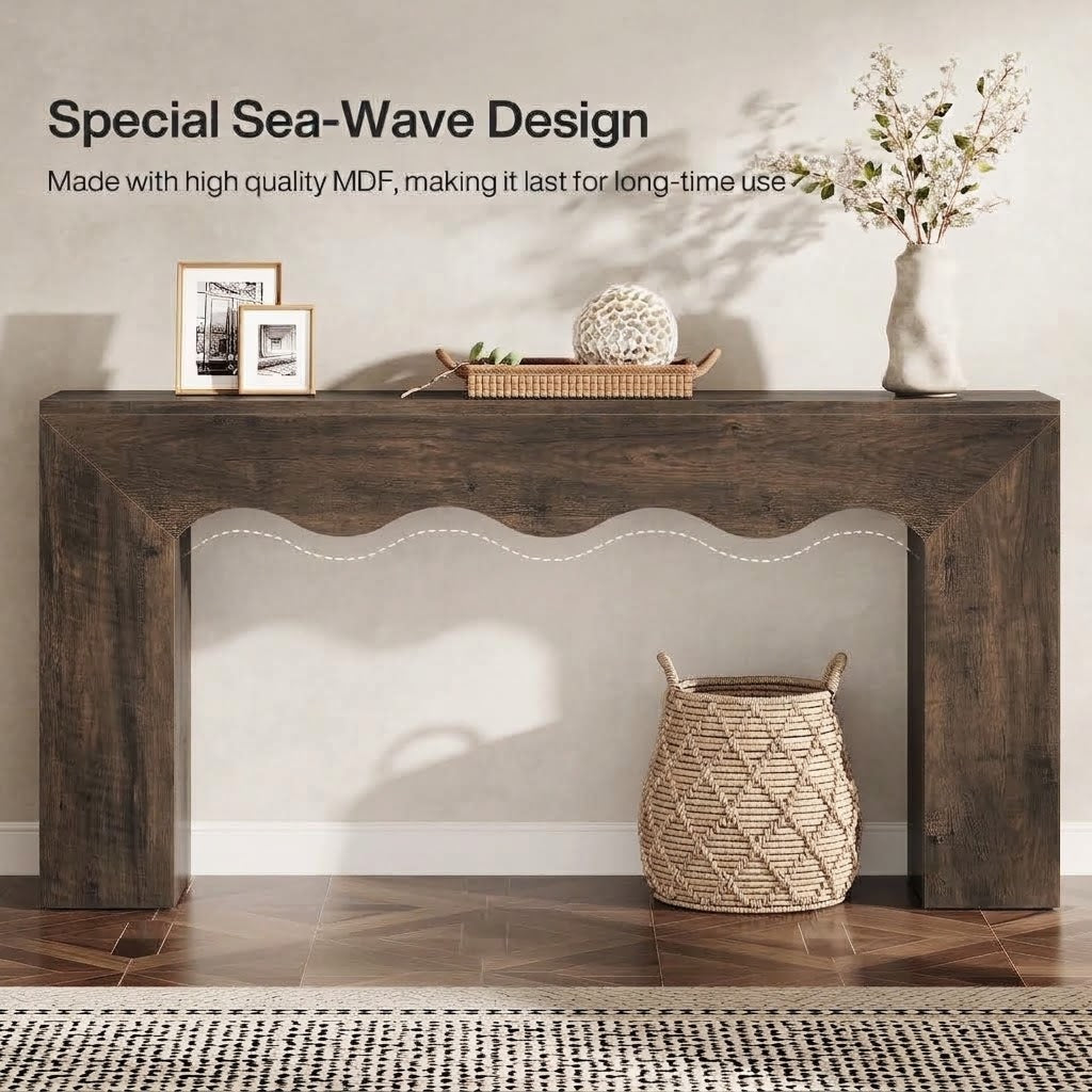 A rustic dark brown MDF console table with a scalloped apron detail, styled in a home entryway setting with decorative items, a vase of flowers, and a woven basket on a wood floor.