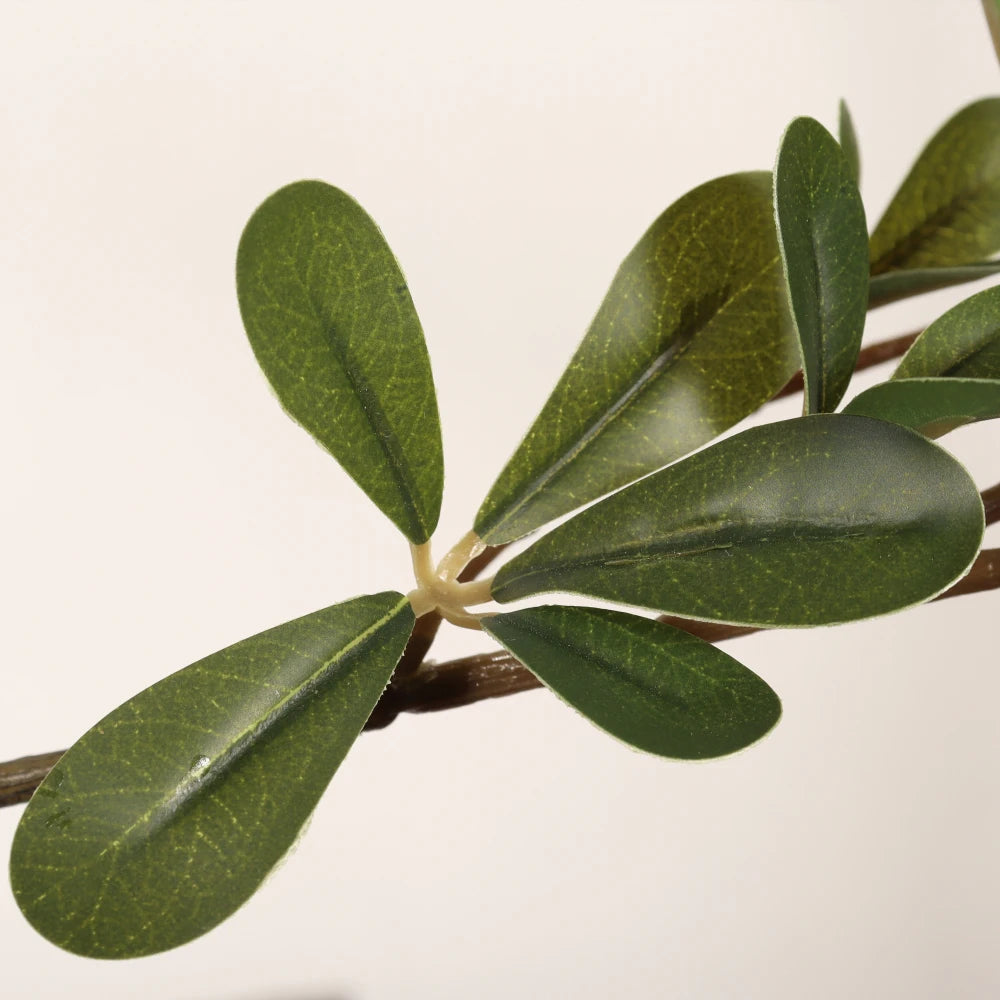 Close-up of an artificial olive branch with green leaves on a light background
