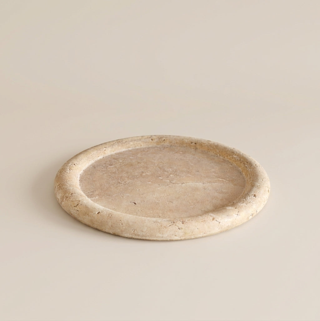 A round, shallow stone tray with a thick, textured rim, shown on a solid, warm beige background.