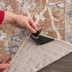 Person adding a black rug corner gripper on a patterned rug.