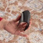 Black rug pad held in a hand against a patterned carpet background