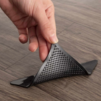 Hand holding a black triangular object with perforated design on a wooden surface