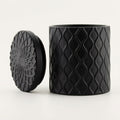 Forbidden Masculine Scent — Matte Black Textured Ceramic Candle with Lid, shown on a clean white background. The container features a raised wavy diamond pattern, and the lid displays a matching embossed floral or sunburst design.