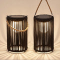 Two black rope lanterns with solar panel tops and rope handles, shown lit against a warm beige background with dramatic shadow rays.