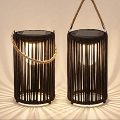 Two black rope lanterns with solar panel tops and rope handles, shown lit against a warm beige background with dramatic shadow rays.