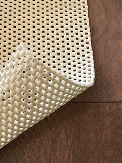 Close-up of a textured beige rug pad on a wooden floor