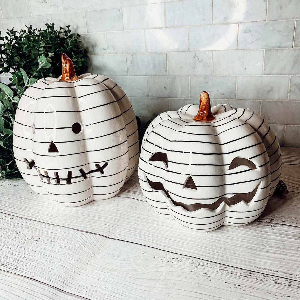 Two decorative pumpkins with black line art and carved faces on a wooden surface.