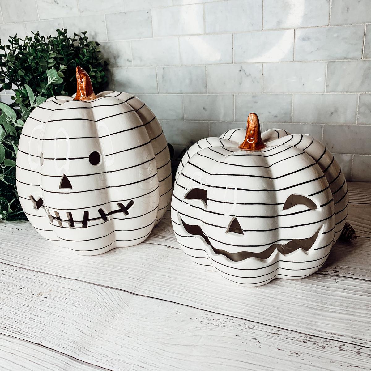 Two decorative pumpkins with black line art and carved faces on a wooden surface.