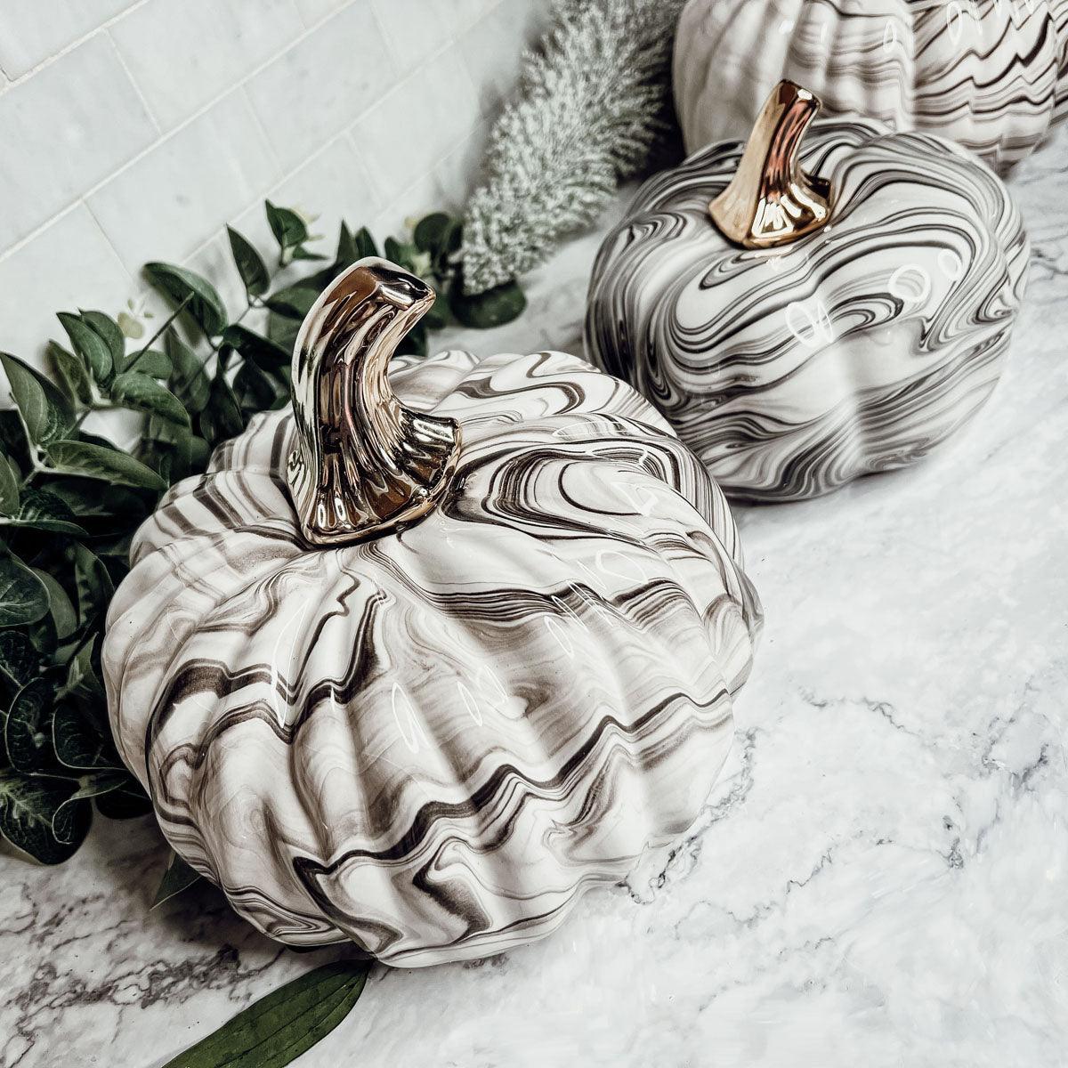 Marble-patterned ceramic pumpkins with gold accents on a marble surface.