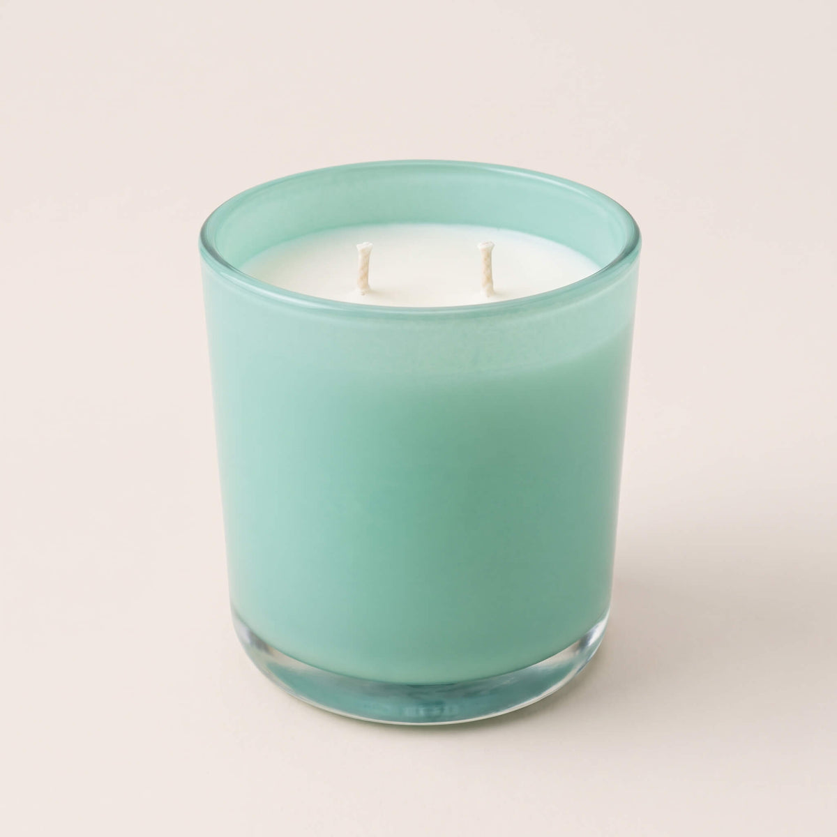 A two-wick scented candle in a frosted mint green glass jar, set against a solid light beige background.