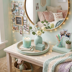 A styled bedroom corner with a light wood vanity table, round mirror, pastel bedding, string lights, a mint candle, flowers in a vase, and small decor accessories. No person is present, but a real interior environment is clearly shown, so this is Lifestyle rather than Product/Packaging.