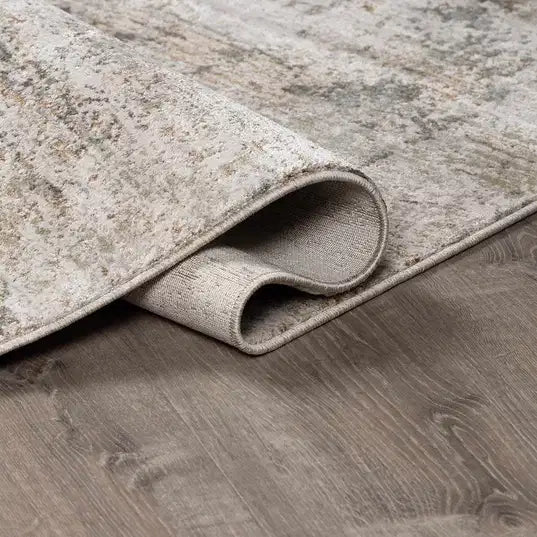 Rolled-up beige  Meral Thick Luxe Boutique Rug on a wooden floor
