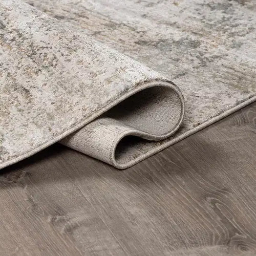 Rolled-up beige  Meral Thick Luxe Boutique Rug on a wooden floor