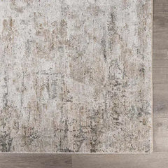 A close-up of a distressed  Meral Thick Luxe Boutique Rug with an abstract, vintage-style pattern in beige, gray, and muted brown tones, shown on a light wood floor.
