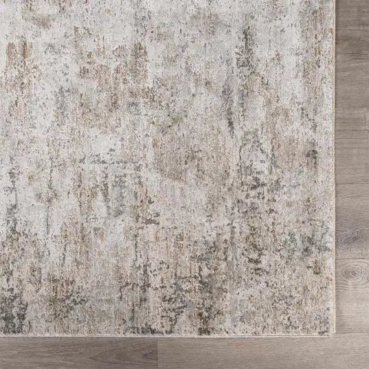 A close-up of a distressed  Meral Thick Luxe Boutique Rug with an abstract, vintage-style pattern in beige, gray, and muted brown tones, shown on a light wood floor.