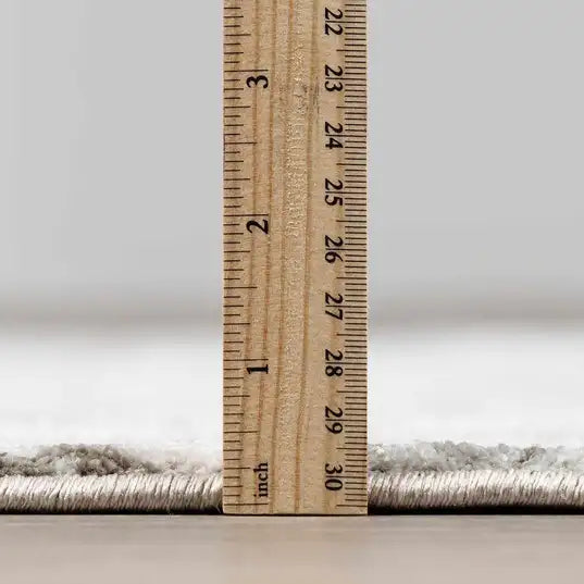 A close-up of a medium pile  Meral Thick Luxe Boutique Rug with a wooden ruler standing vertically to show the pile height and texture, set against a neutral gray background.