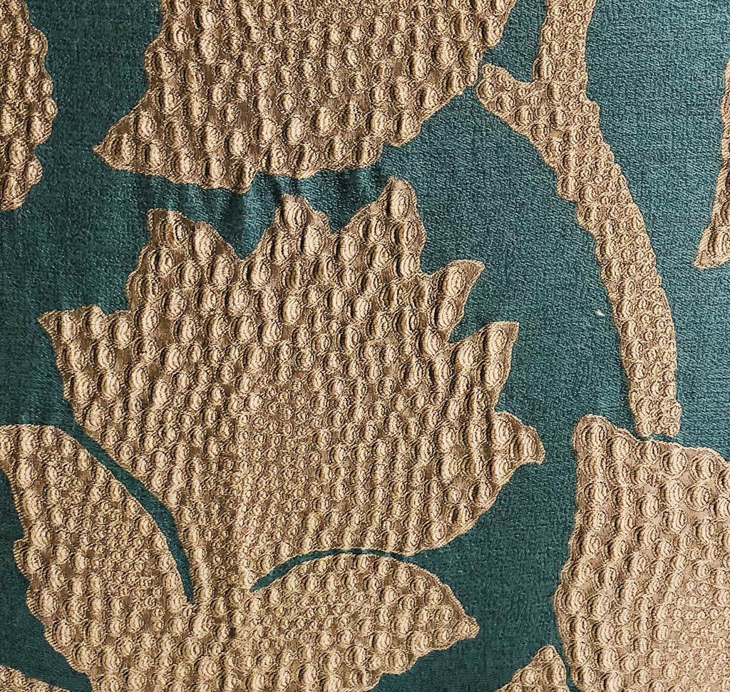 Close-up of a textured throw pillow's gold leaves on a teal background