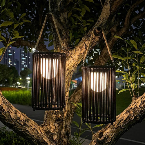 Two black woven solar lanterns hanging from a tree