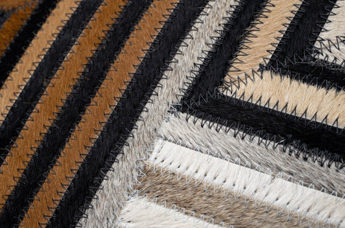 Close-up of a textured cowhide throw pillow fabric with diagonal stripes and chevron in brown, black, and beige.