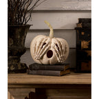 Decorative pumpkin with skeleton hands on a wooden surface