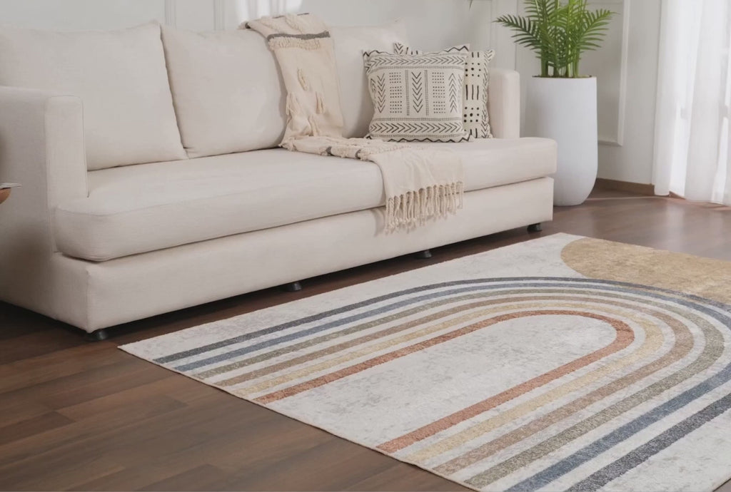 A product video for the Giza Contemporary Washable Multicolor Rainbow Area Rug. The clip begins with a macro close-up highlighting the durable, medium-pile polyester texture and vibrant navy, rust, and mustard tones. It then showcases the rug beautifully styled on light wood floors in a child's playroom and a neutral-toned baby nursery, demonstrating its versatile design.