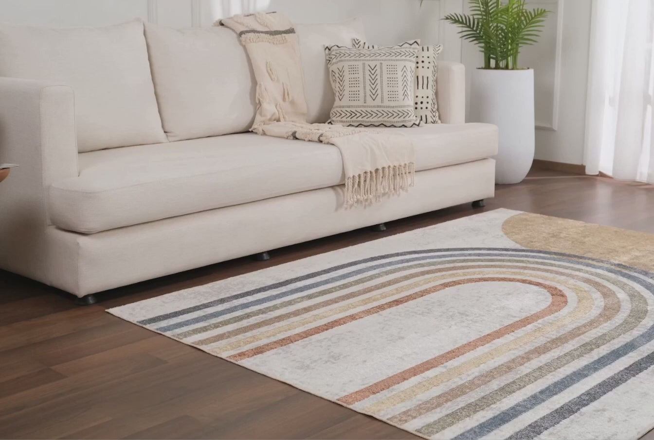 A product video for the Giza Contemporary Washable Multicolor Rainbow Area Rug. The clip begins with a macro close-up highlighting the durable, medium-pile polyester texture and vibrant navy, rust, and mustard tones. It then showcases the rug beautifully styled on light wood floors in a child's playroom and a neutral-toned baby nursery, demonstrating its versatile design.
